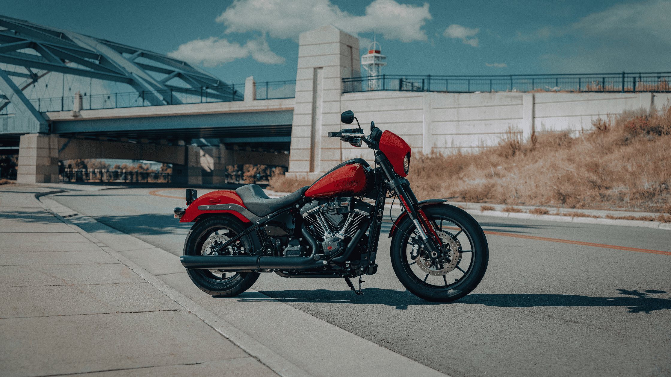 2025 H-D® Low Rider® S in striking red finish parked curbside near bridge with urban backdrop