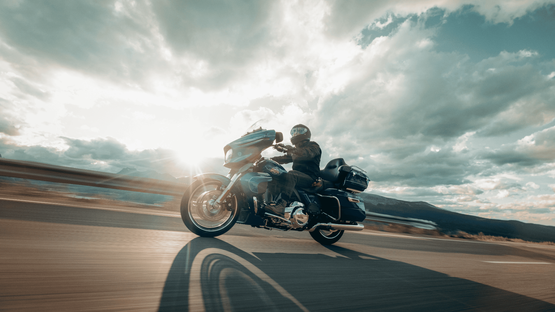 Rider on 2025 Street Glide Ultra cruising highway at sunset with scenic mountains and cloudy skies.