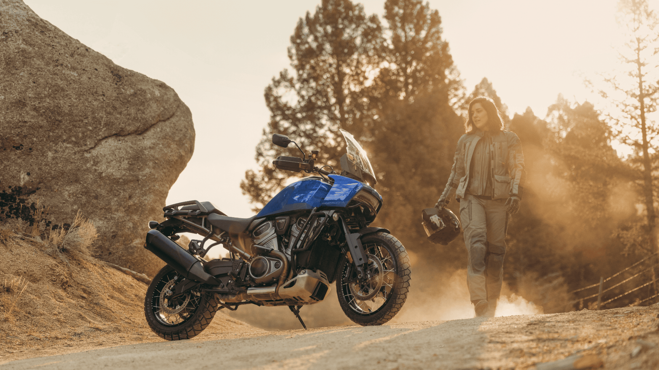 2025 Harley-Davidson® Pan America® 1250 Special in blue parked on a dirt trail with a rider beside i…