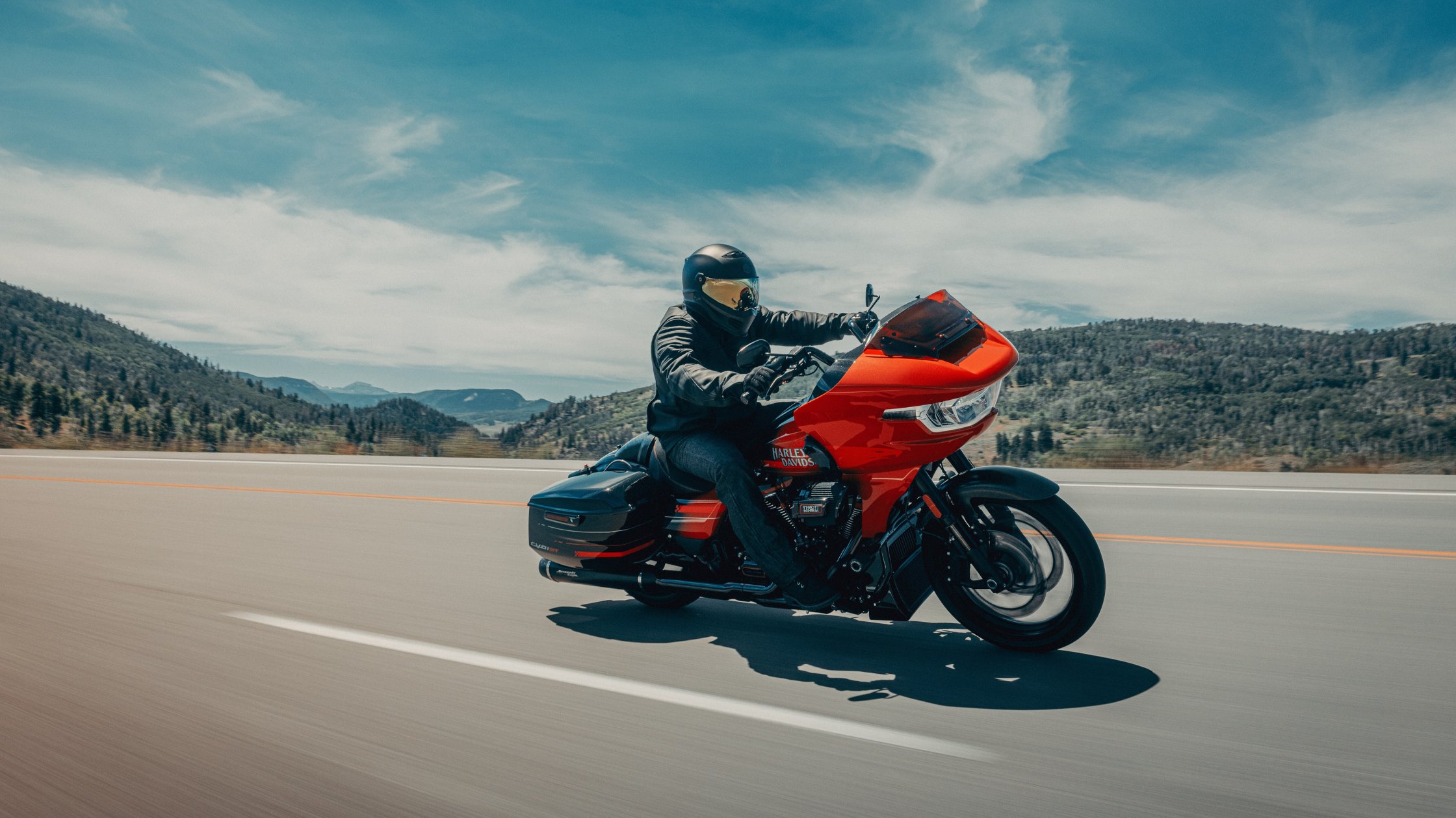 Red 2026 H-D® CVO™ Road Glide® ST ridden on an open highway with hills and blue sky in the background