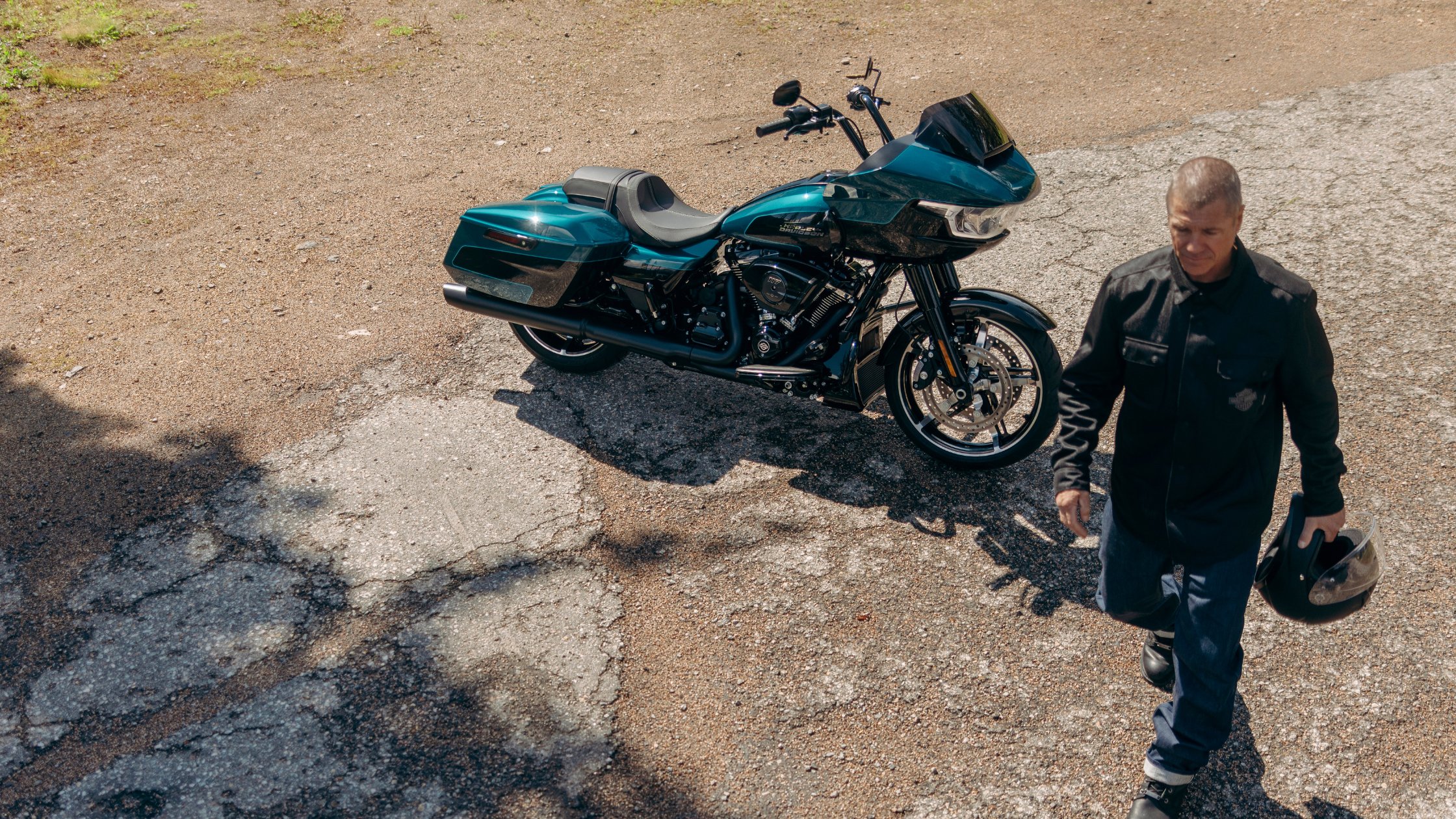 Rider walking past teal 2026 Harley-Davidson® Road Glide® touring motorcycle with hard saddlebags