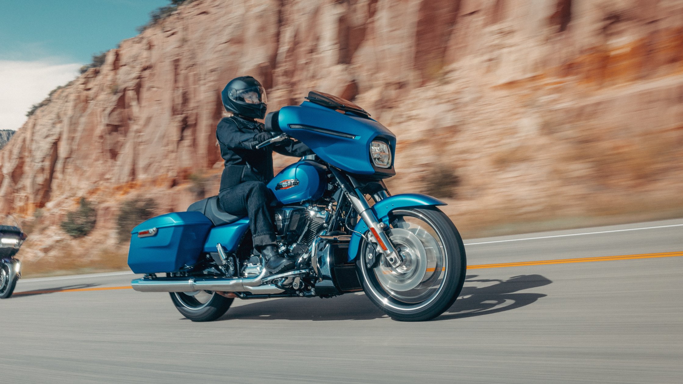 Rider cruising blue 2026 Harley-Davidson® Street Glide® on open highway beside red rock canyon