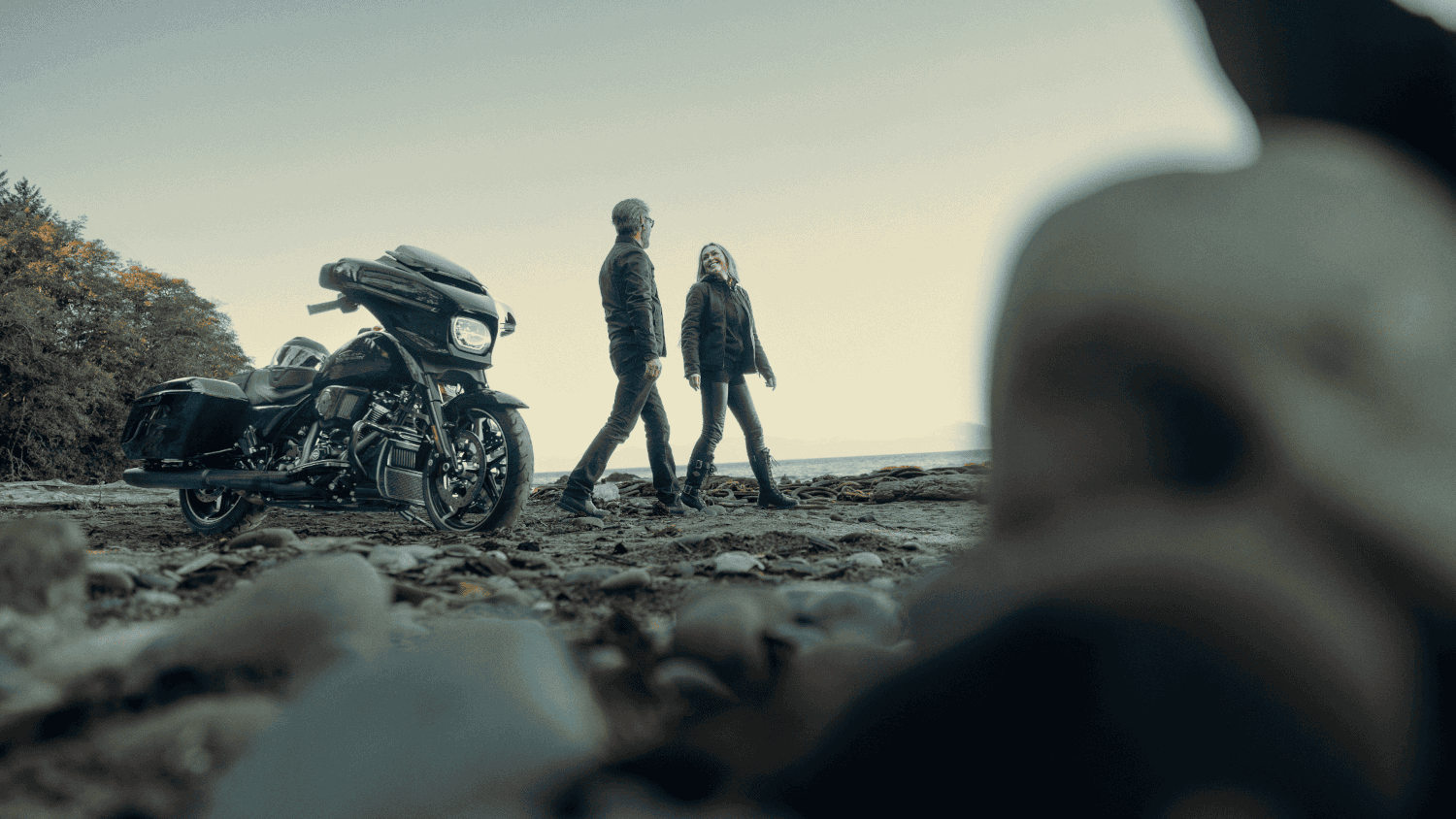 Couple walks on a rocky shore with a 2024 Harley-Davidson&reg; Street Glide&reg; parked in the foreground